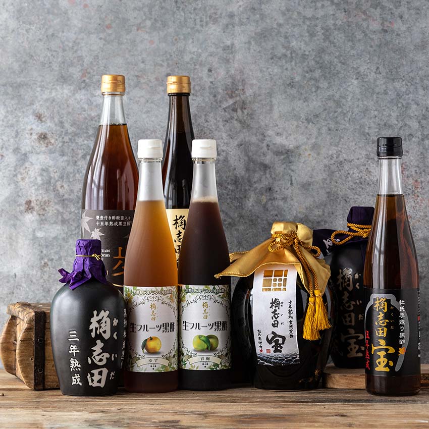 A selection of eight Japanese liqueur bottles of various shapes and sizes, with different colored labels and decorative packaging, displayed against a gray textured background.