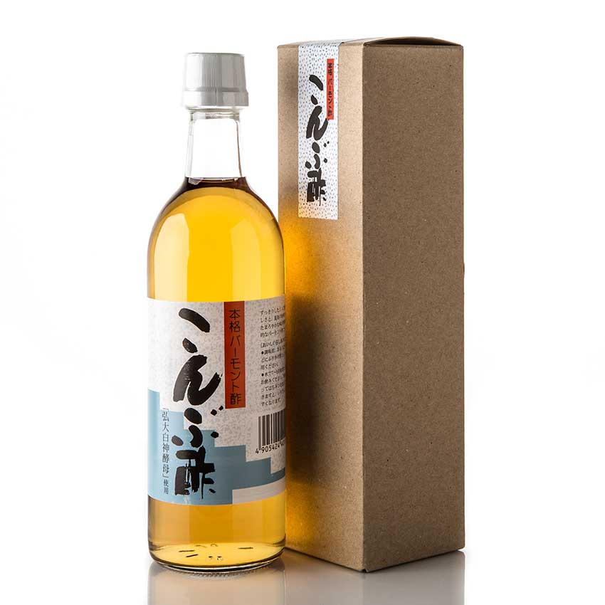 A glass bottle with a white label containing amber liquid, placed next to a tall brown cardboard box, both featuring Japanese text.