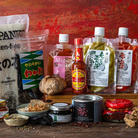 A variety of Japanese and Asian food ingredients, sauces, spices, and condiments arranged on a wooden surface against a red background.