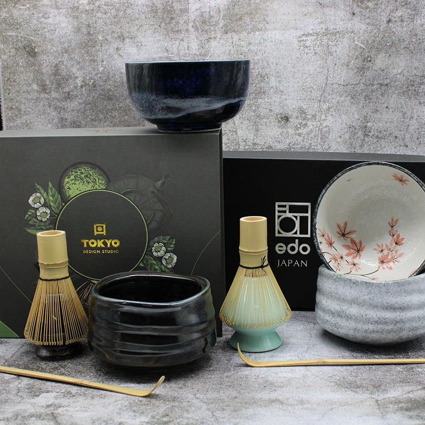 Ceramic matcha bowls, bamboo whisks, and boxed sets from Tokyo Design Studio and Edo Japan displayed on a textured surface.