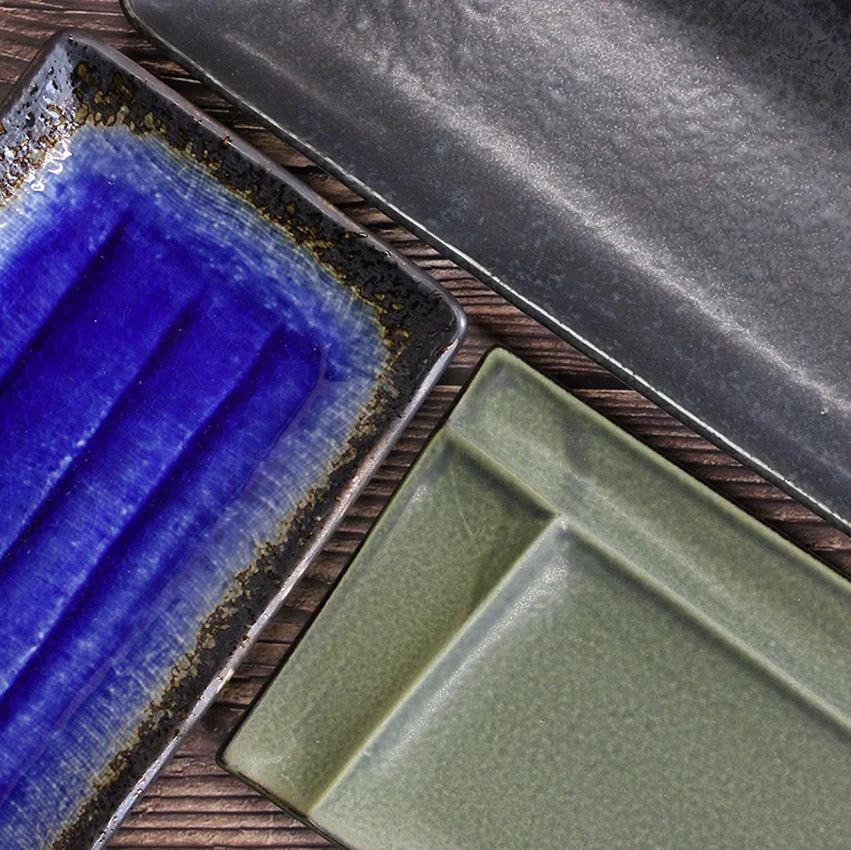 Three rectangular ceramic plates—one blue, one gray, and one green—arranged on a wooden surface.
