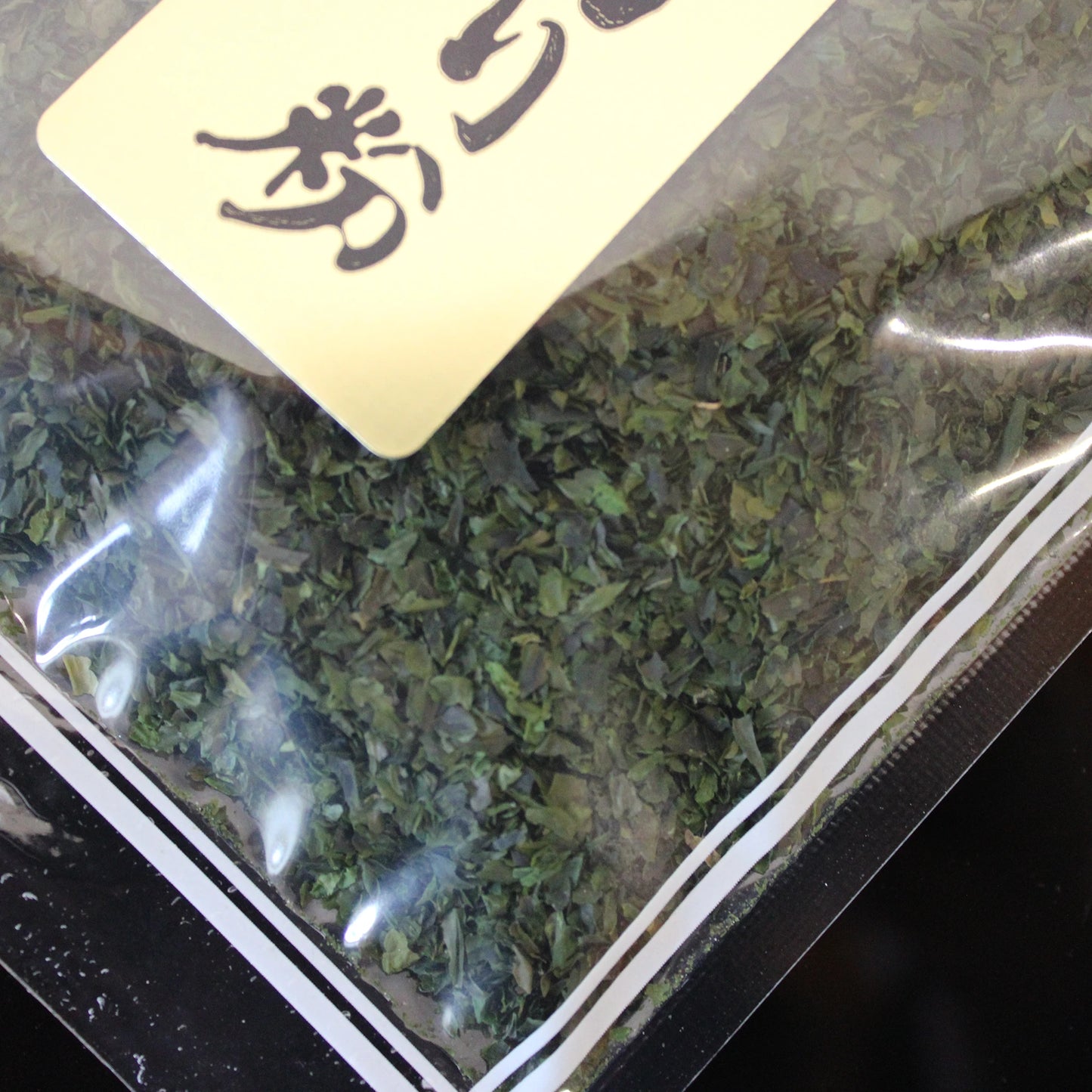 A close-up of a sealed bag labeled Dried Aonori Seaweed Flakes - 20g with Japanese text, containing dried green aonori flakes—an essential ingredient in Japanese cuisine.