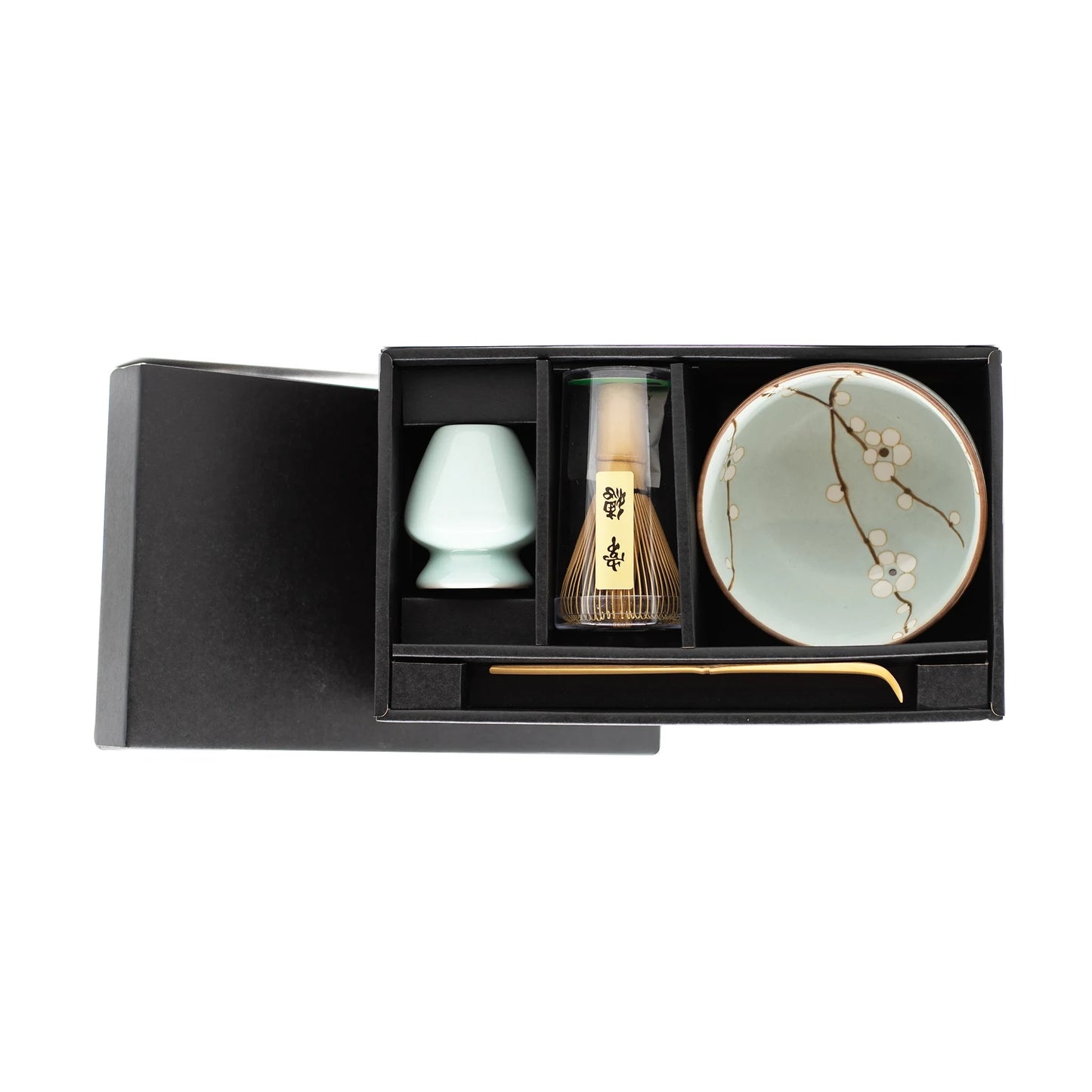 The Matcha Tea Set - Cherry Blossom comes in a black box with a floral bowl, bamboo whisk, scoop, and holder—essentials for Japanese tea making—neatly arranged in separate compartments.
