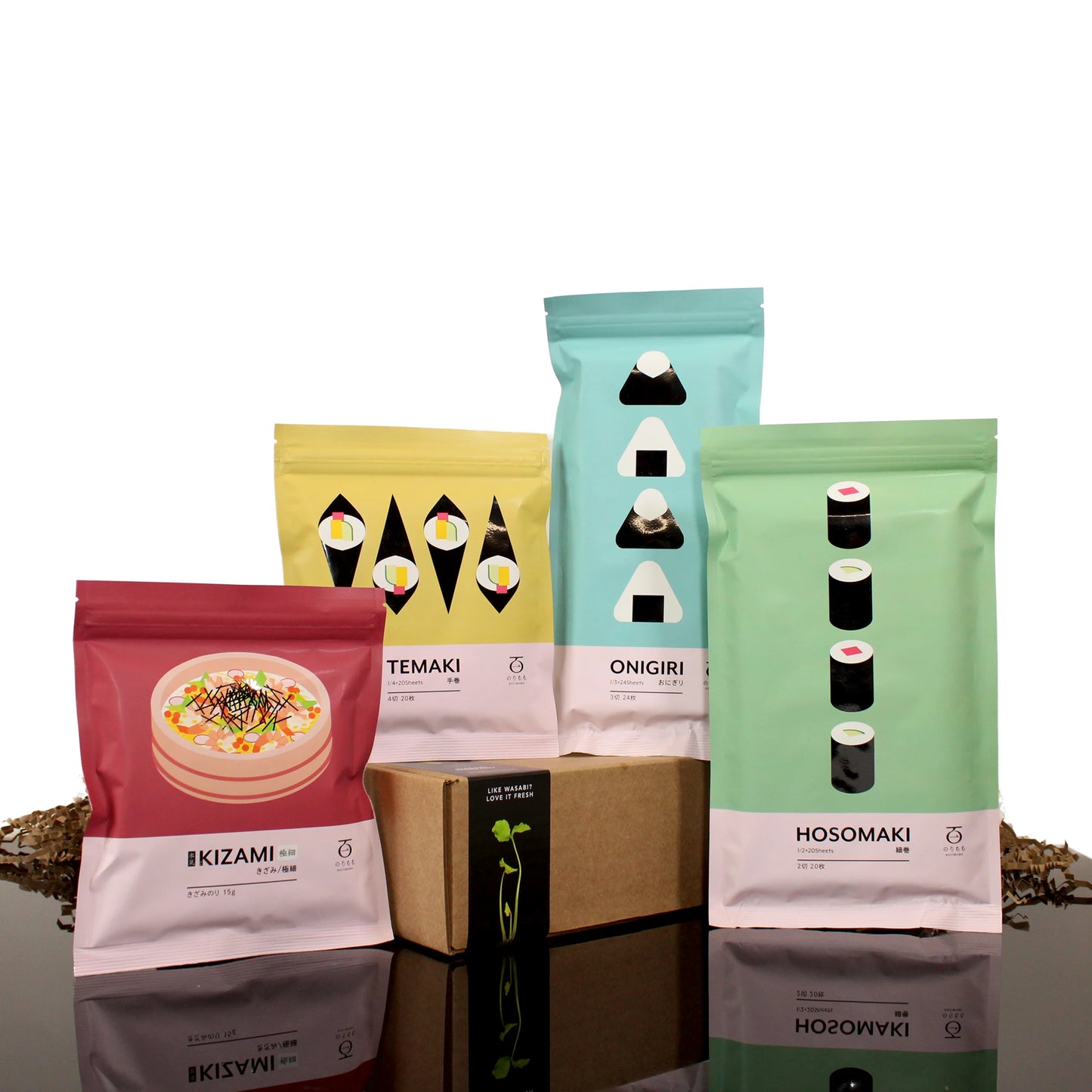 Four vibrant MomoFuku Nori Set packages with minimalist sushi roll art surround a small brown box on a reflective surface with scattered brown pebbles, evoking the taste of delicious seaweed.
