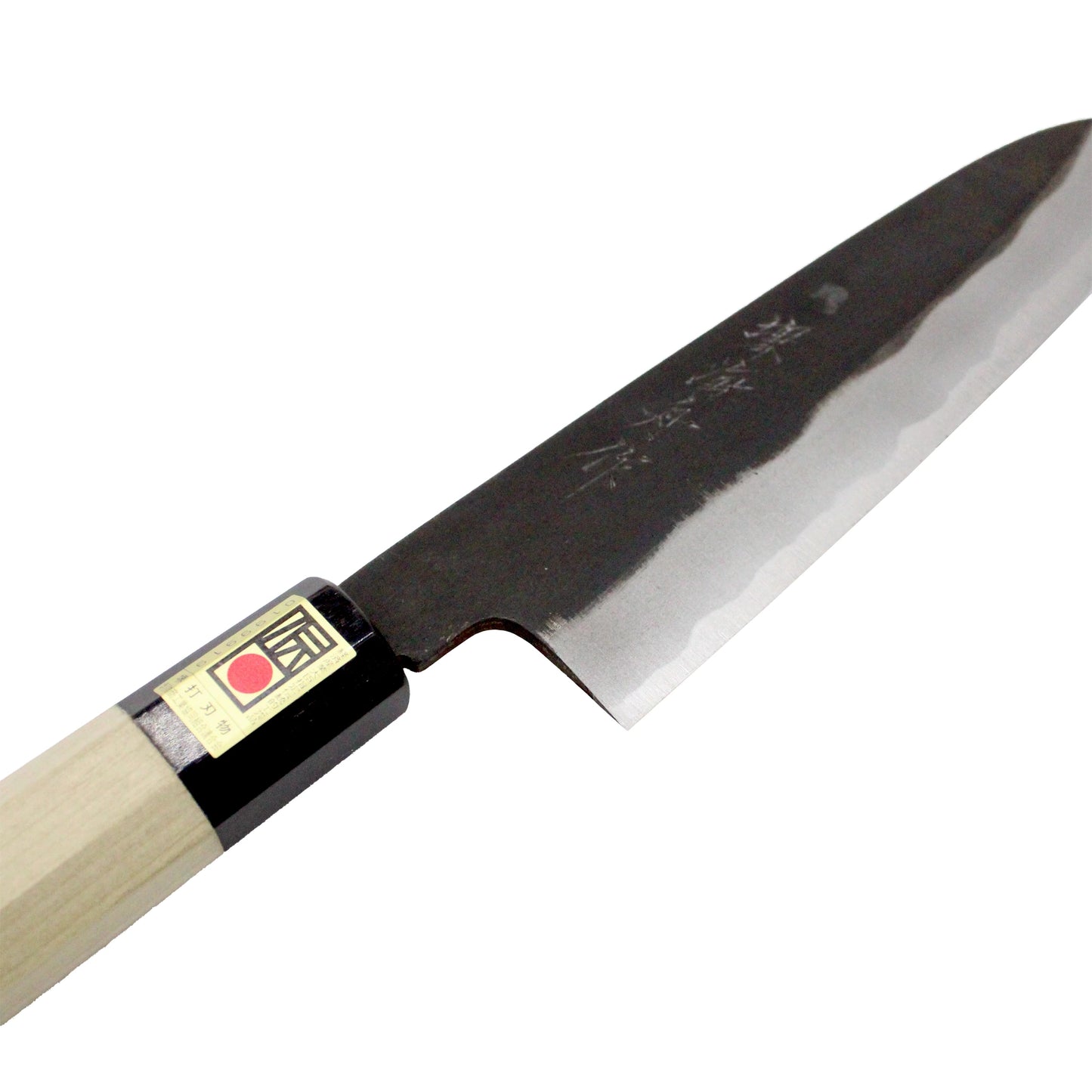 The Gyuto Chef’s Knife Black Forged 210mm is a Japanese kitchen knife with a sharp double-bevel edge, engraved characters on its black blade, and a light wooden handle with a label near the grip.