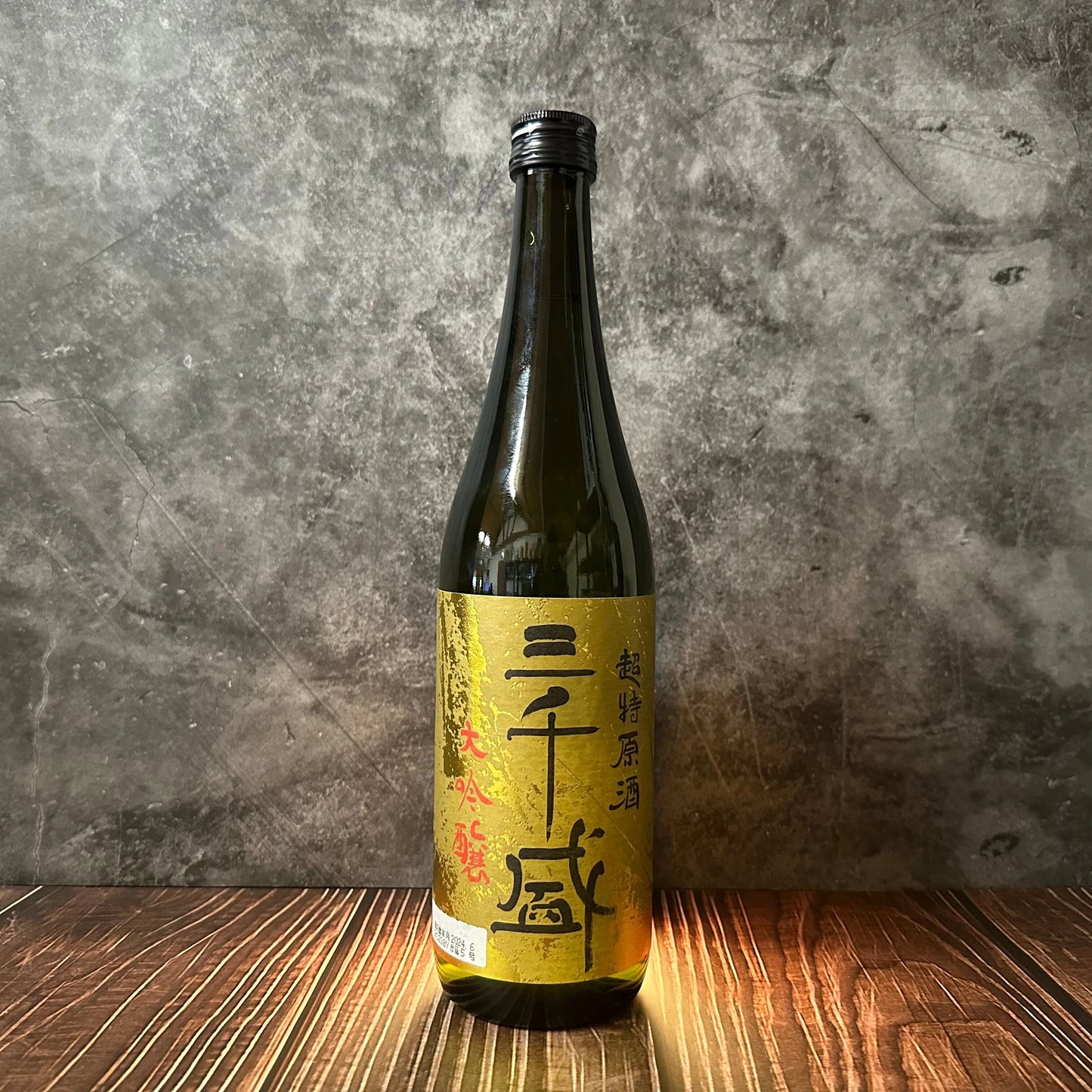 A bottle of Chotoku Heavenly Brew - Honjozo (Genshu) Sake, adorned with a gold and black Japanese label, rests on wood before a stone-textured backdrop, showcasing this sake’s versatile and refined elegance.