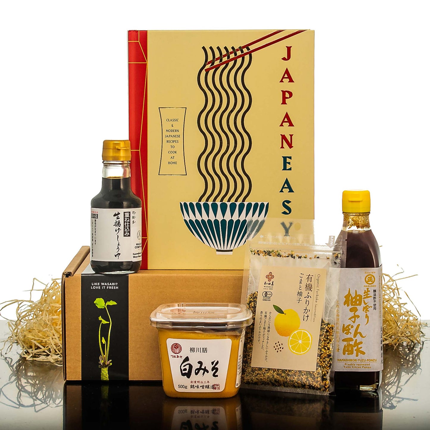 The Japanese Cooking Starter Set with JapanEasy Cook Book includes soy sauce, yuzu seasoning, white miso paste, and seasoning mix—everything you need to discover authentic umami flavors, beautifully arranged on shredded paper.