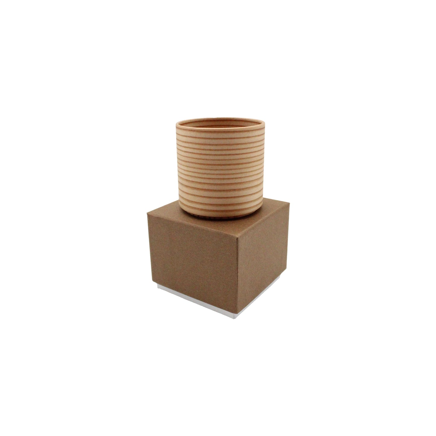 The Sake Cup - Bent Wood, a cylindrical cedarwood cup with horizontal grooves, rests atop a closed brown cardboard box against a white background.