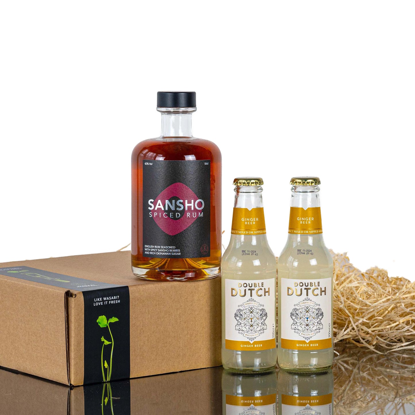 The Sansho Rum & Double Dutch Ginger Beer Set includes a bottle of Sansho Spiced Rum, two Double Dutch Ginger Beers, and a brown gift box, beautifully arranged on a white background.