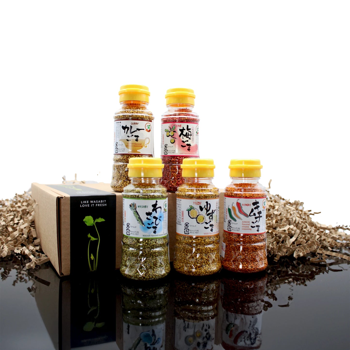 The Sesame Seeds 5 Flavours Set is displayed with five bottles next to a gift box on a reflective surface, with decorative shredded paper in the background.