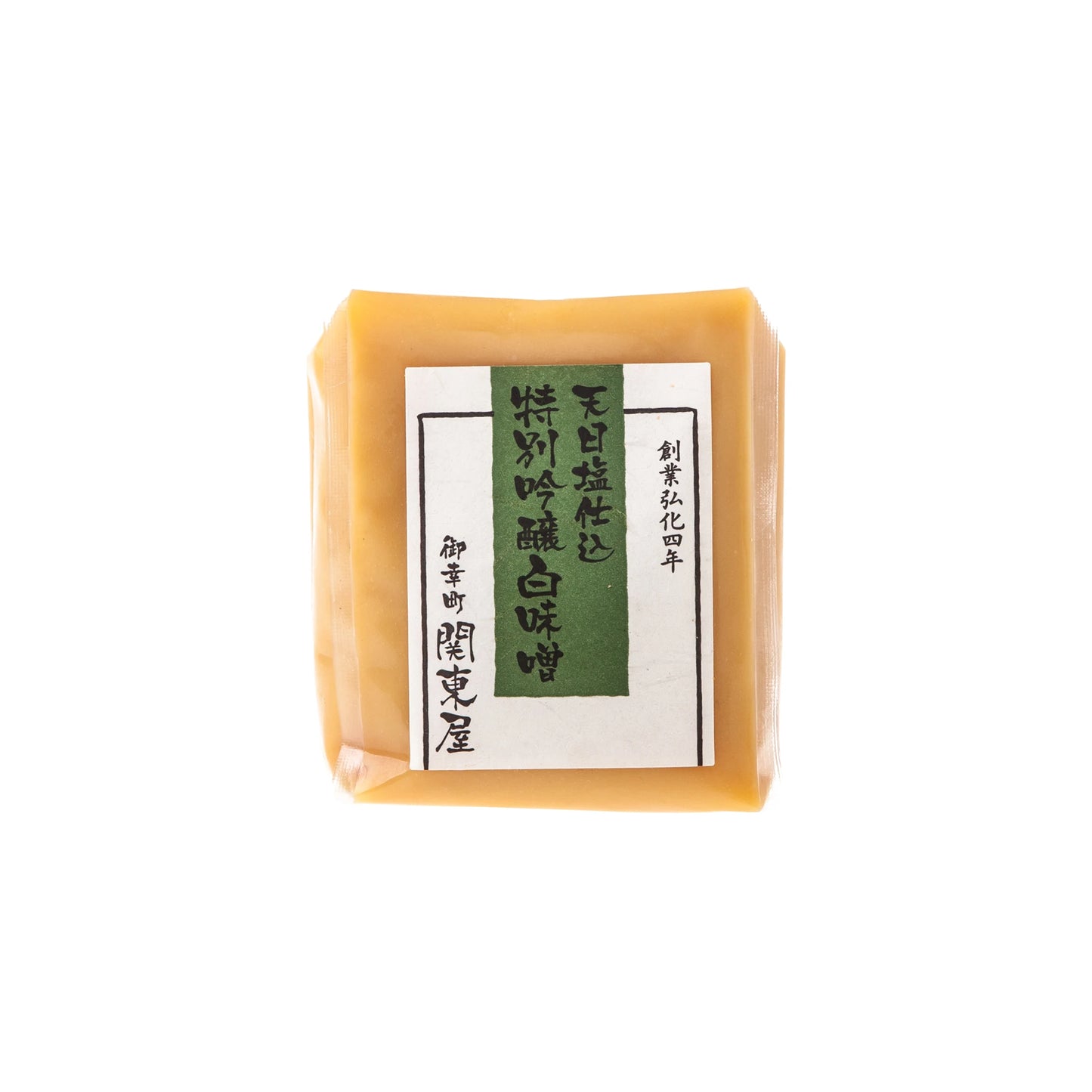 A block of Shiro White Miso in a clear plastic package with a white and green label featuring Japanese text, highlighting the traditional fermentation process essential to Japanese cuisine.