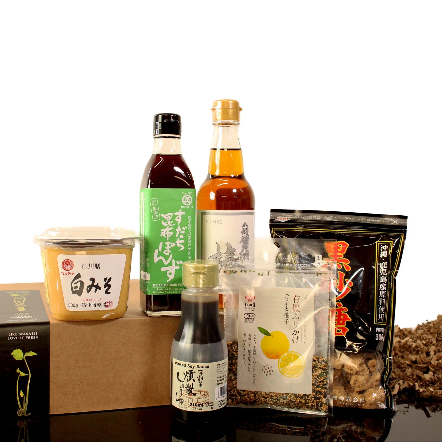 The Ultimate Vegan Japanese Cooking Collection, featuring ponzu sauce, white miso paste, seasonings, and dried mushrooms for vegan Japanese cuisine, is displayed on a reflective surface.