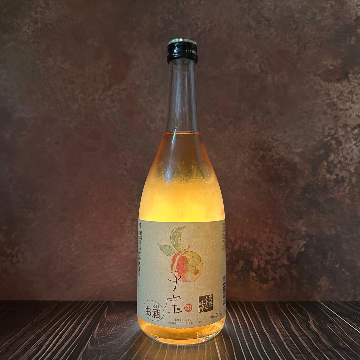 A 720ml glass bottle of Umeshu Plum Sake, featuring a black cap and plum illustration, rests on a dark wooden surface with a textured brown background, evoking the look of a classic Japanese aperitif.