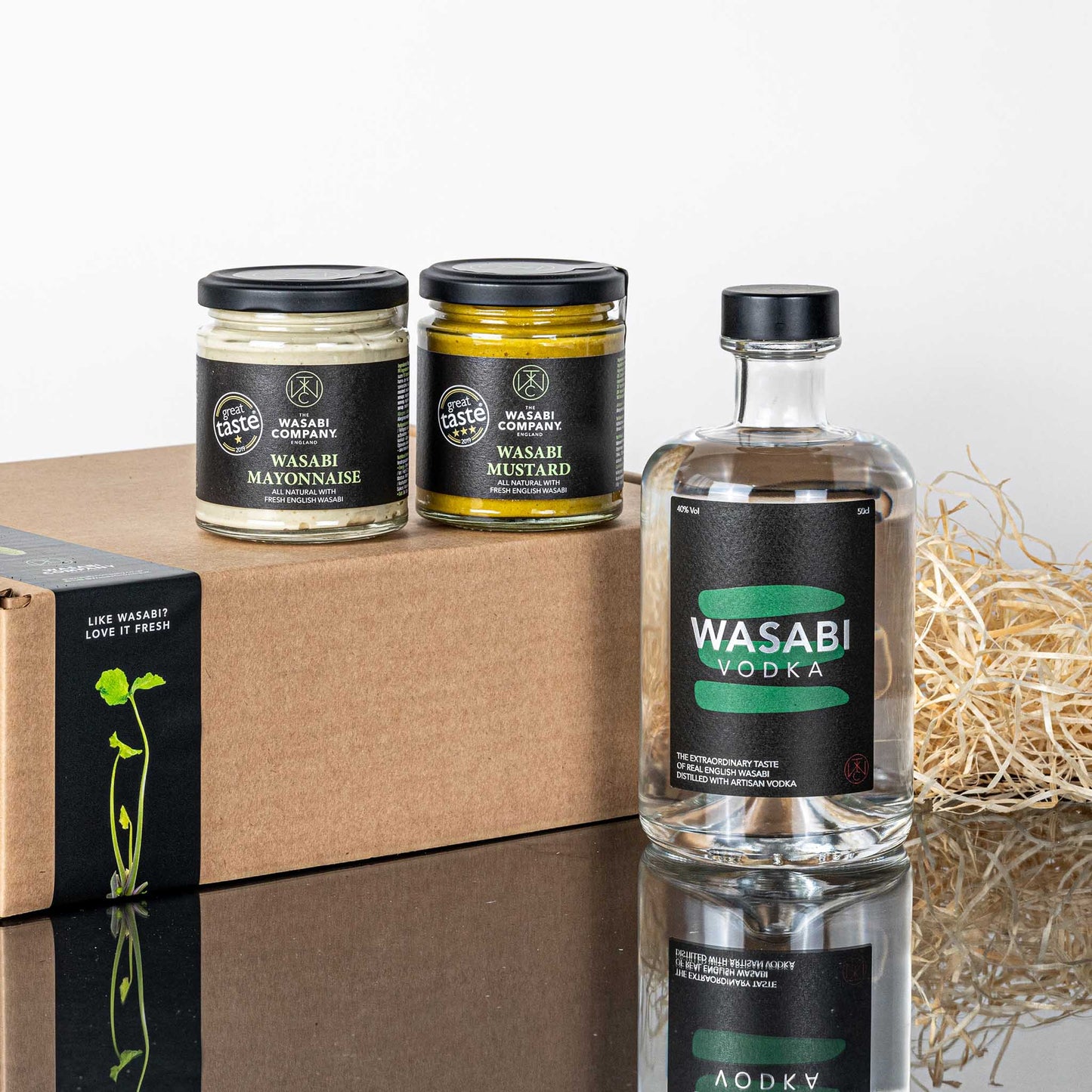 The Wasabi Freaks Collection, featuring wasabi mayonnaise, wasabi mustard, and wasabi vodka, is displayed next to a brown cardboard box with packing straw.