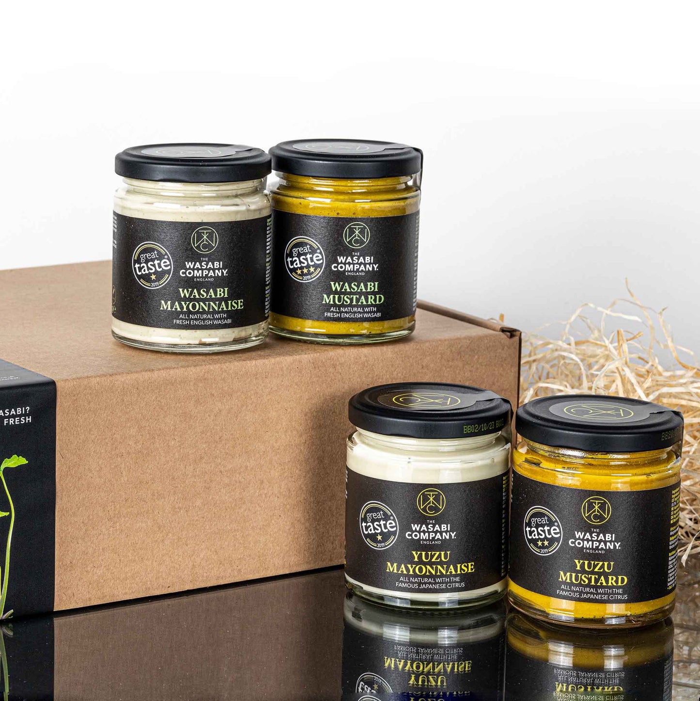 The Wasabi & Yuzu Mayo & Mustard Full Set—four jars of wasabi mayonnaise, wasabi mustard, yuzu mayonnaise, and yuzu citrus mustard—is displayed on and beside a cardboard box with straw packaging material nearby.