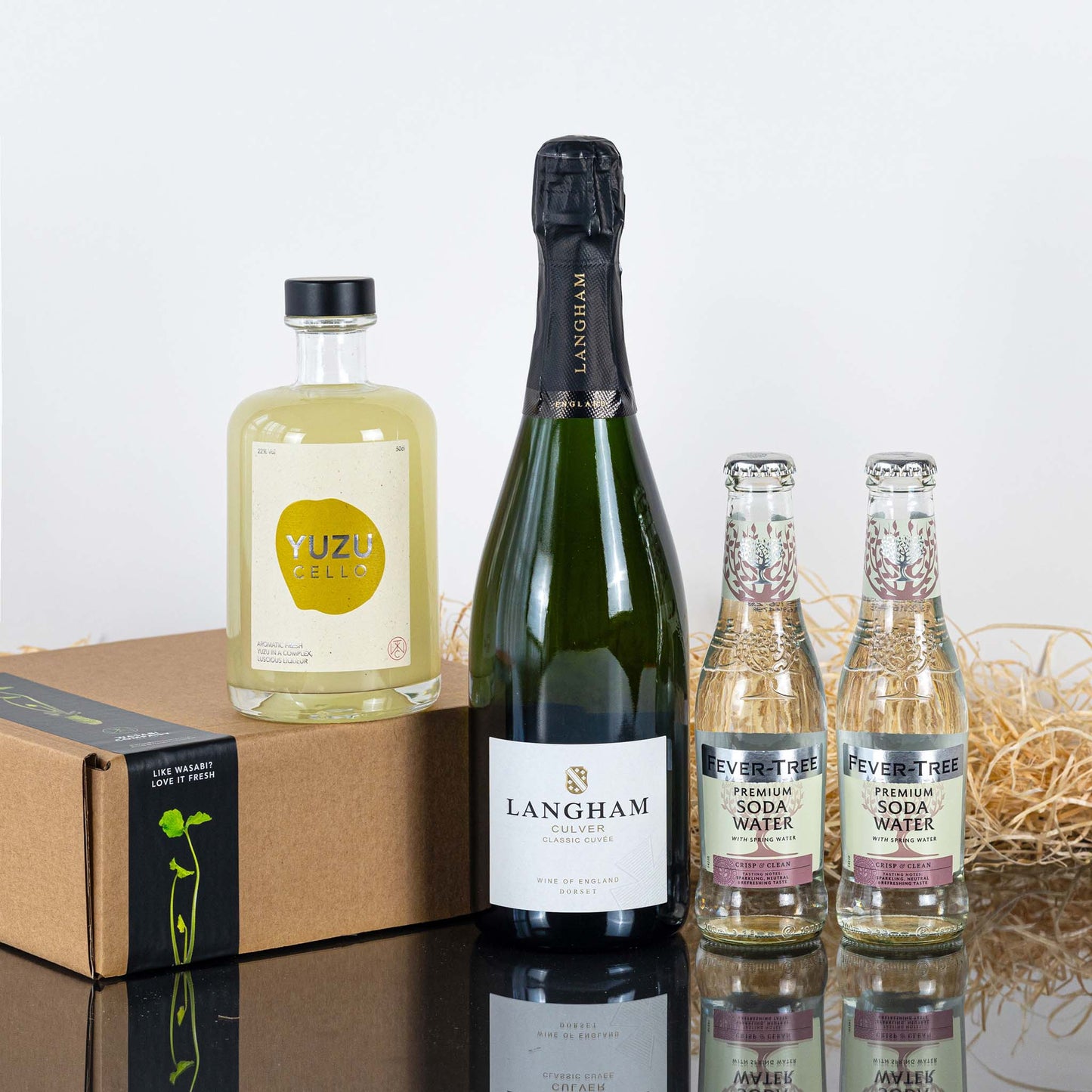 The Yuzucello Spritz Cocktail Set is displayed with a bottle of Yuzucello, sparkling wine, and two Fever-Tree Soda Waters beside a straw-filled cardboard box.