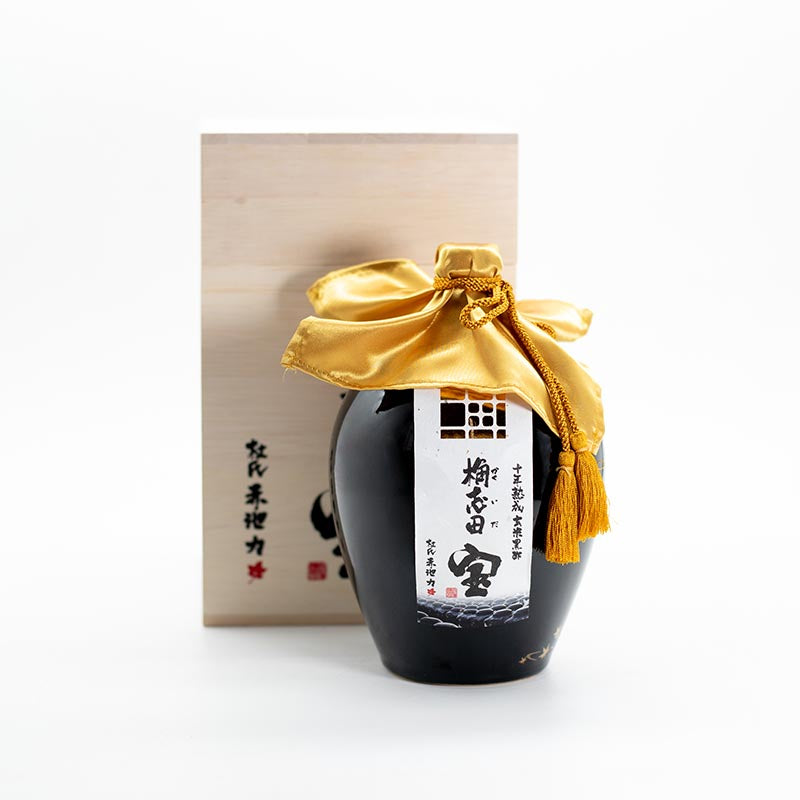 A 1L bottle of 10 Year Aged Black Rice Vinegar with a gold cloth cover and tassel, featuring Japanese text, sits before a wooden box with more Japanese writing—part of the Kagoshima Kinko Bay Treasure Kashida collection.