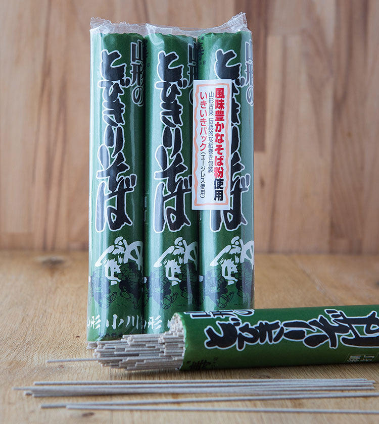 Three packages of Soba Noodles (3 x 150g) in green packaging are shown on a wooden surface, with some noodles partially visible from an opened pack in the foreground.