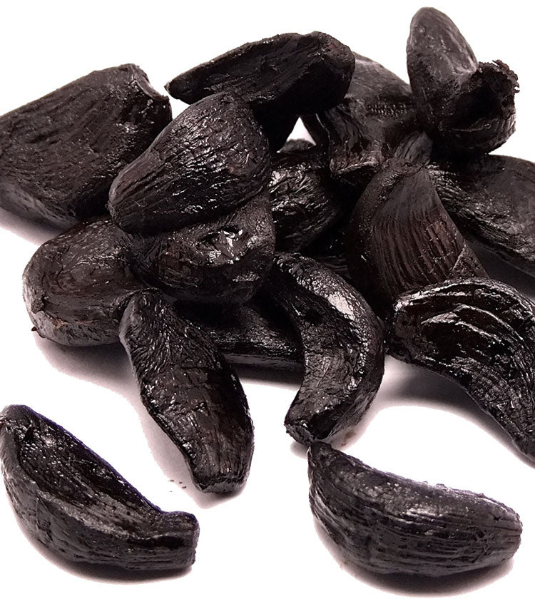Black Garlic (Peeled Cloves) - 50g is shown as a glossy, dark pile on a white background, emphasizing its balsamic vinegar flavor and versatility as a seasoning.