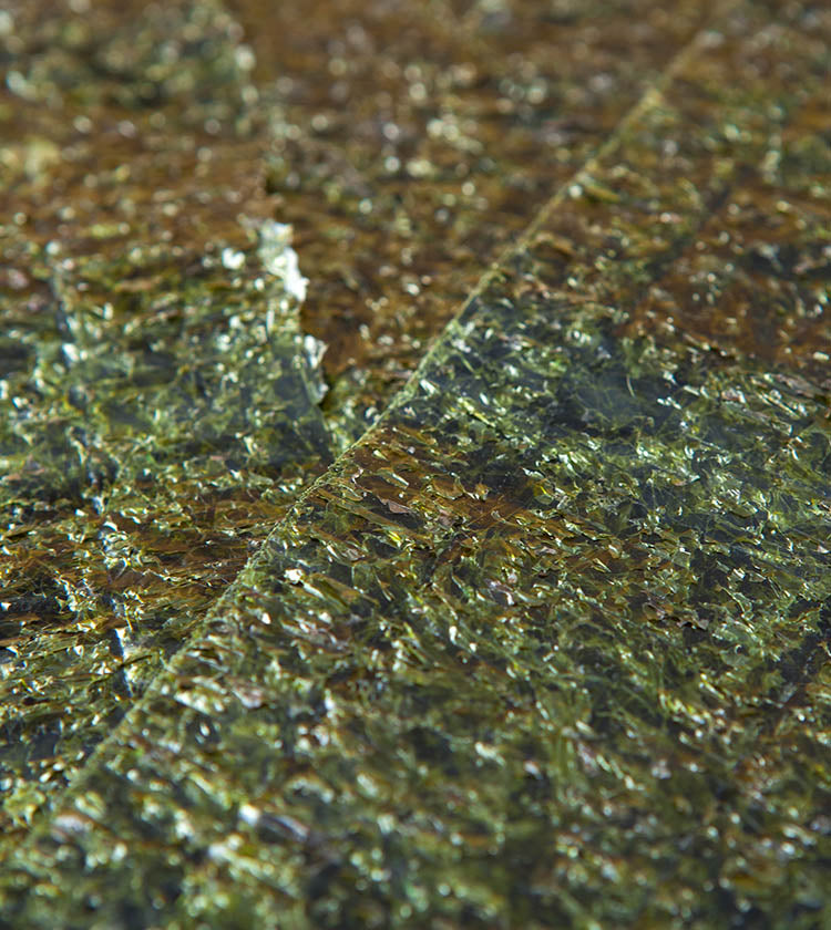 Close-up view of several overlapping Sanpuku Roasted Nori sheets, highlighting their shiny, textured, and dark green surface. Each pack contains 10 premium-quality sheets.