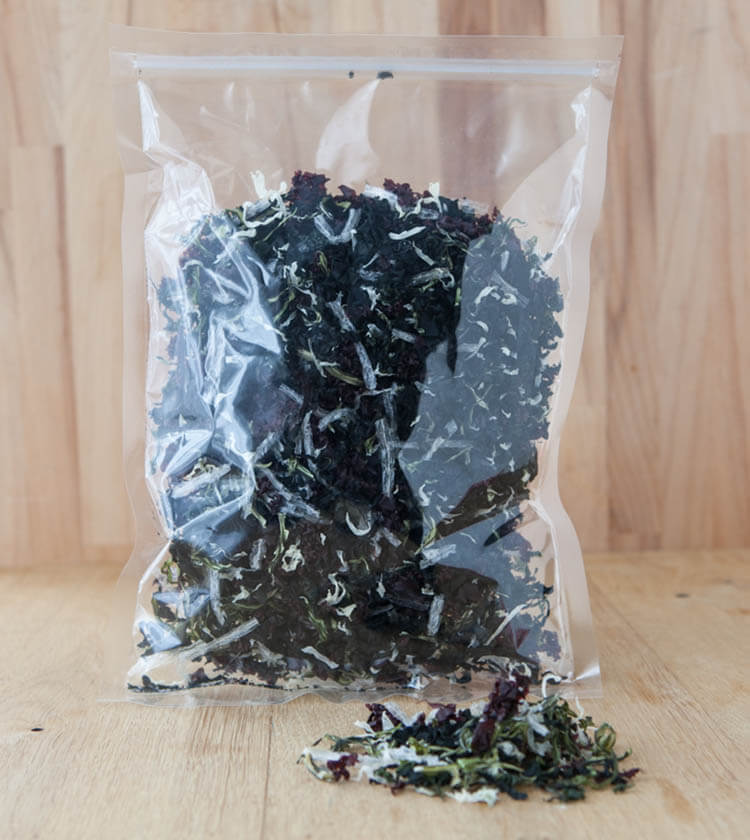 A clear plastic bag of Superior Seaweed Salad rests on a wooden surface, with a small pile of these nutrient-rich seaweeds spilling out in front.
