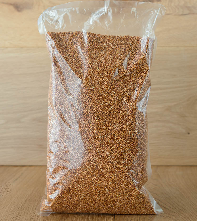 A clear plastic bag of Sesame Seeds with Kimchi sits upright on a wooden surface against a light wood background, perfect for adding to your favorite noodles or homemade kimchi.
