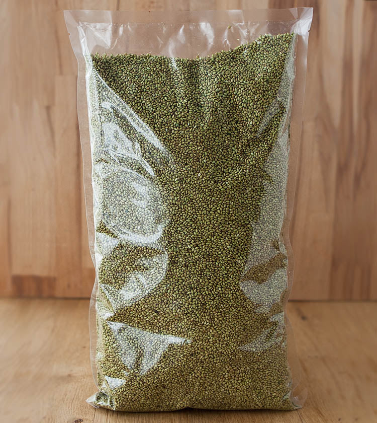A clear plastic bag labeled Sesame Seeds with Wasabi, filled with green mung beans and sesame seeds, stands upright on a wooden surface against a wooden background.