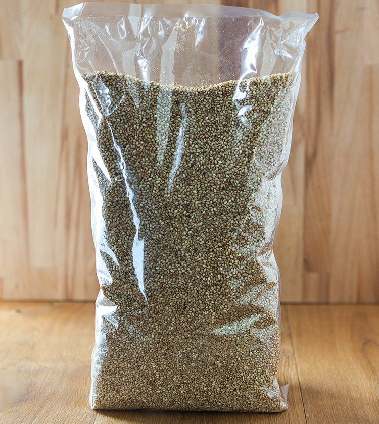 A clear plastic bag of Sesame Seeds with Yuzu stands upright on a wooden surface, accompanied by uncooked quinoa, all set against a wood background.