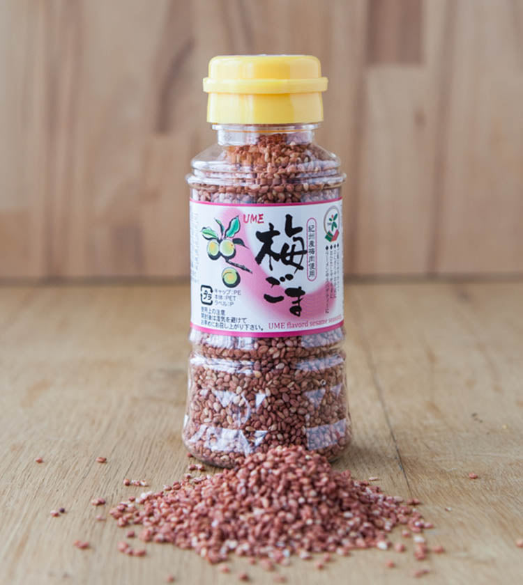 A bottle of Sesame Seeds with Ume Plum sits on a wooden surface with some seeds spilled in front.