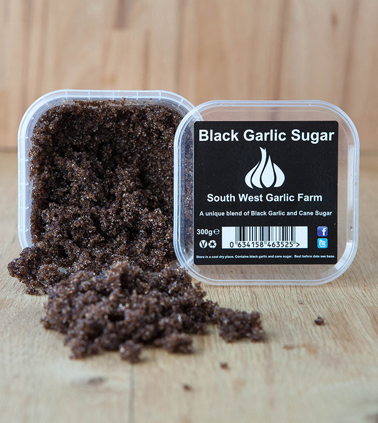 A 300g plastic container of Black Garlic Sugar, with some of the contents spilled onto a wooden surface.