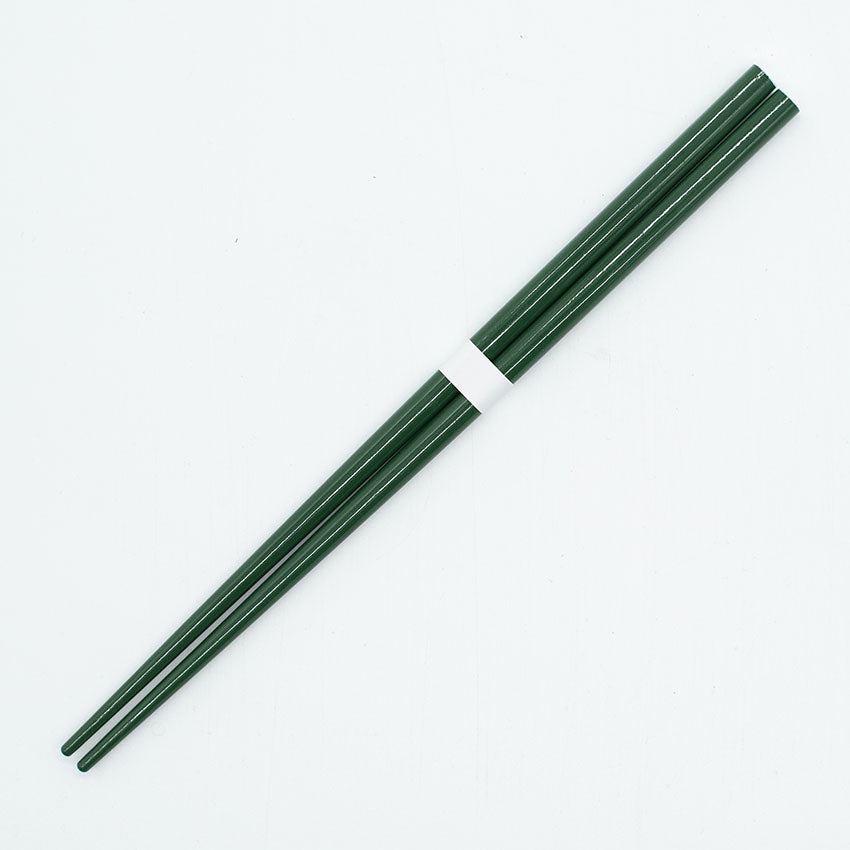 A pair of Chopsticks - Deep Green lies parallel on a light surface, secured by a white band, highlighting the refined artistry of traditional lacquerware.
