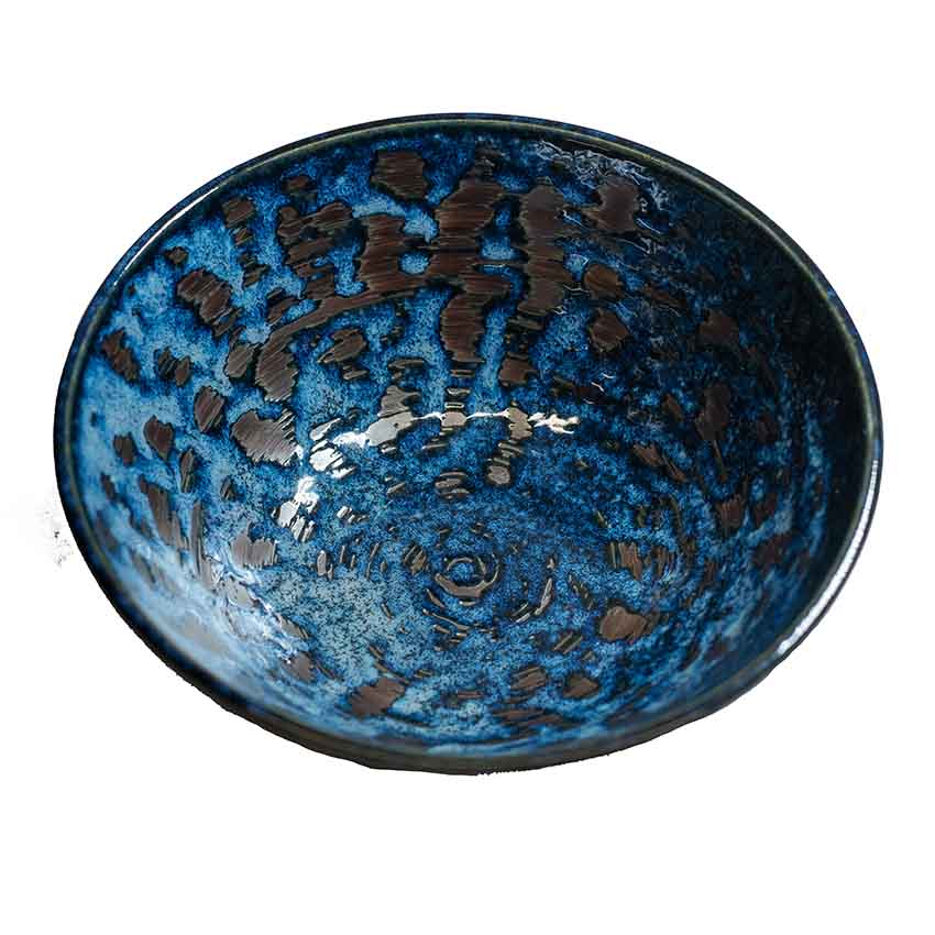 The Udon Bowl - Copper Swirl is a round Minoyaki porcelain bowl with a glossy blue glaze and irregular dark brown spots and patterns on the interior.