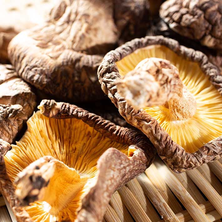Close-up of Dried Organic Koshin Shiitake Mushrooms 42-75mm (70g), showing visible gills as they rest on a woven bamboo surface.
