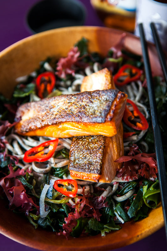 Superior Seaweed Salad features grilled salmon fillets on noodles, mixed seaweeds, sliced red chili peppers, and vegetables, served with chopsticks resting on the bowl.