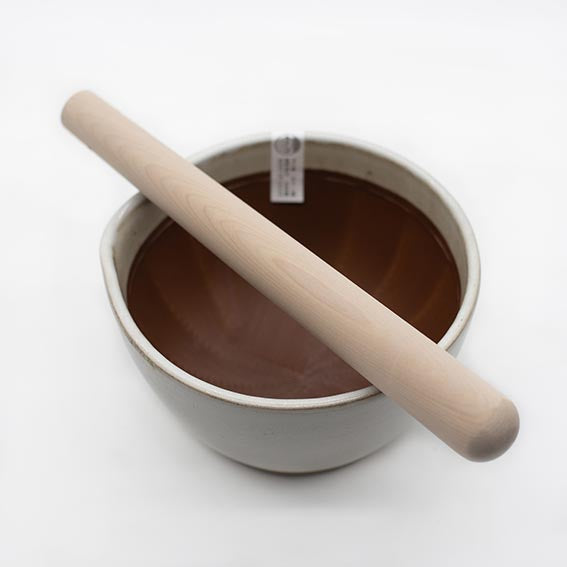 The Suribachi Motoshige, Pestle & Mortar - White features a white ceramic bowl filled with chocolate liquid, resembling a Japanese earthenware mortar, with its wooden pestle resting across the top.