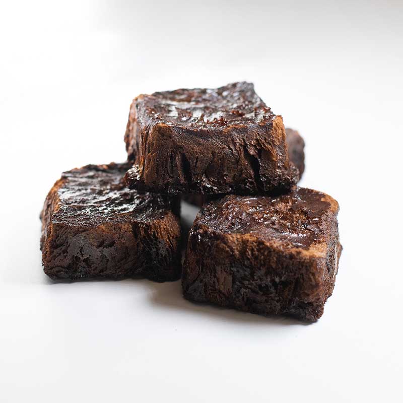 Three pieces of rich, dark chocolate brownies stacked on a white surface, subtly enhanced with the umami depth of 3 Year Aged Soy Freeze Dried 30g.
