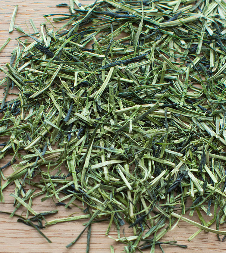 Loose Sencha Karigane Tea leaves (50g) from Comins Tea rest on a wooden surface—fresh, vibrant, and ideal for brewing a focusing cup.