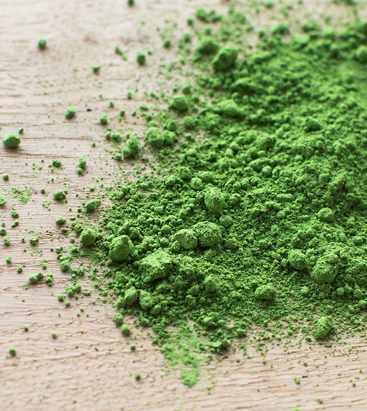 Matcha Superior Tea - 40g, a vibrant and energizing green tea powder, scattered across a light wooden surface.