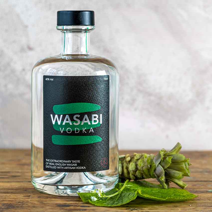 A bottle of Wasabi Vodka - 50cl stands on a surface beside a fresh wasabi rhizome and green leaves, set against a neutral background.