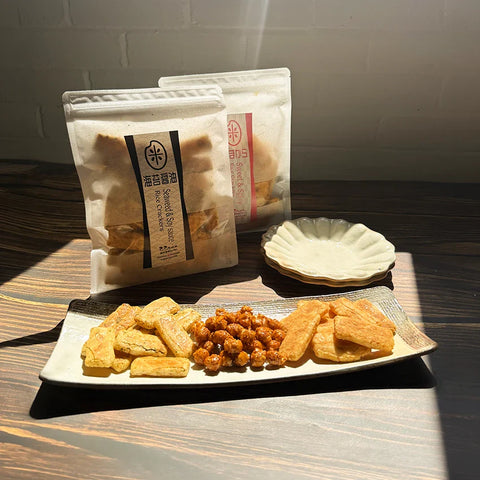 Two packets of Japanese snacks with patterned designs, featuring green and black accents, are placed on a rustic wooden surface.