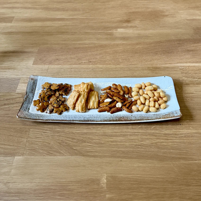 A rectangular plate with four types of assorted Japanese rice crackers arranged in separate sections, placed on a wooden table.