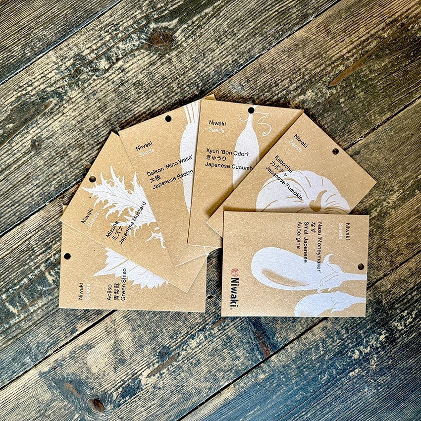 Seven brown Niwaki seed packets with white illustrations and text, arranged in a fan shape on a white background.