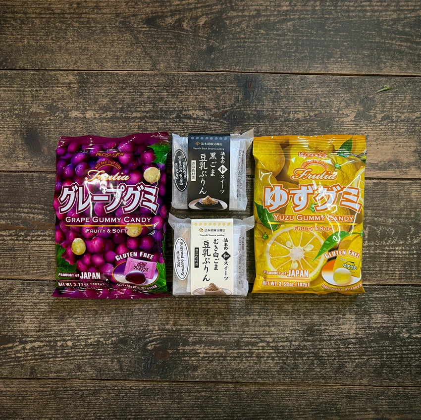 Two bags of Japanese gummy candy, one grape and one yuzu flavor, with two packages of traditional Japanese sweets, all placed on a wooden surface.