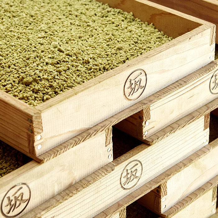 
                  
                    Stacked wooden crates filled with light green grains used to make Ume Kurozu (black rice vinegar with ume plum) - 200 ml, each marked with a circular stamp.
                  
                