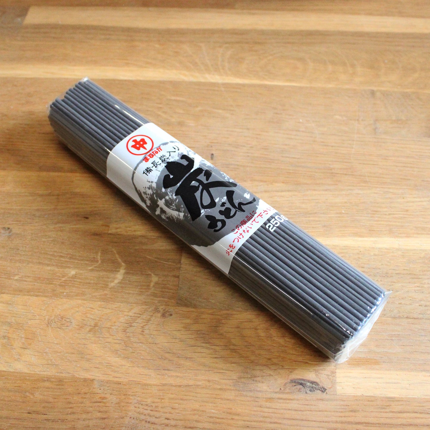 A 250g package of Black Binchotan Udon Noodles wrapped in clear plastic with a white and black label, placed on a wooden surface.