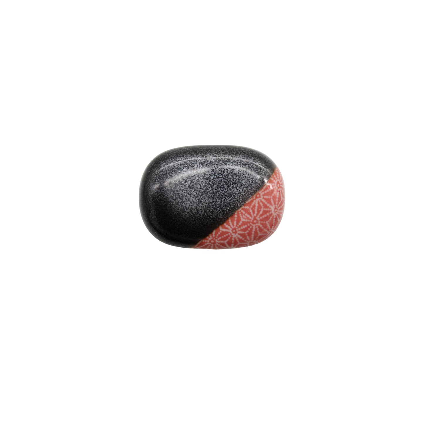 The Chopstick Rest - Pebble Gunmetal Grey & Coral is a smooth, rounded stone with a gunmetal grey finish, black speckles, and a red section adorned with a Japanese star pattern on one side, displayed on a white background.