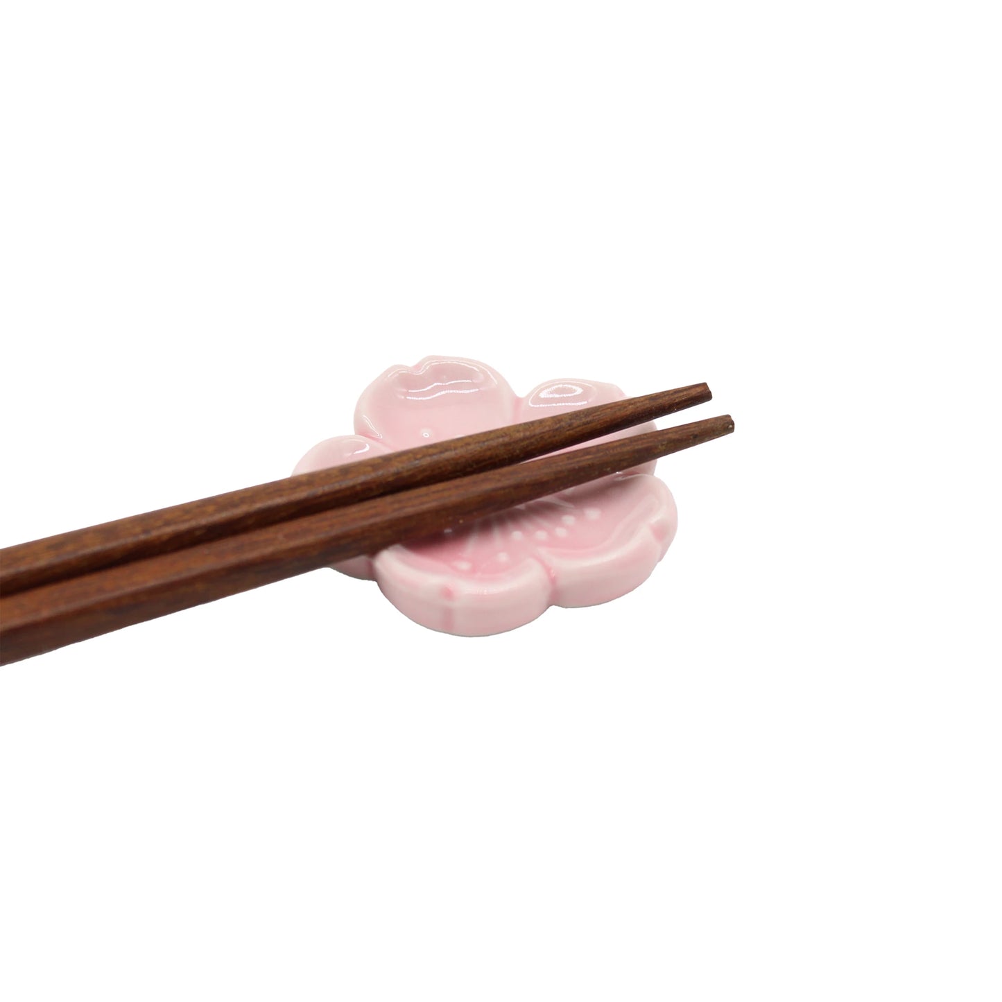 
                  
                    A pair of wooden chopsticks rests on the Chopstick Rest - Pink Sakura, crafted from Minoyaki porcelain and shaped like a pink flower, set against a white background.
                  
                
