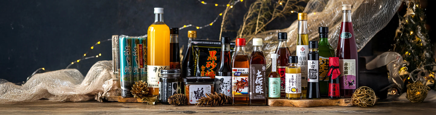 A variety of Japanese condiments, sauces, and seasonings are arranged on a wooden board with festive decorations and warm string lights in the background.