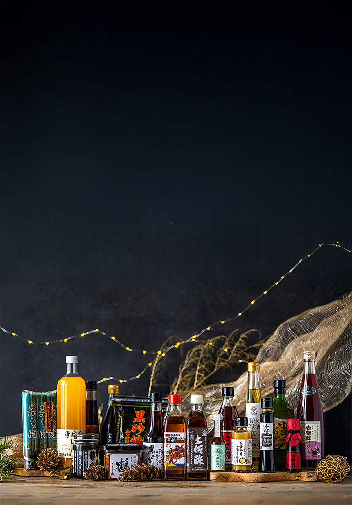 A variety of bottled beverages and packaged food products are arranged on a wooden surface with festive string lights and decorative elements in the background.