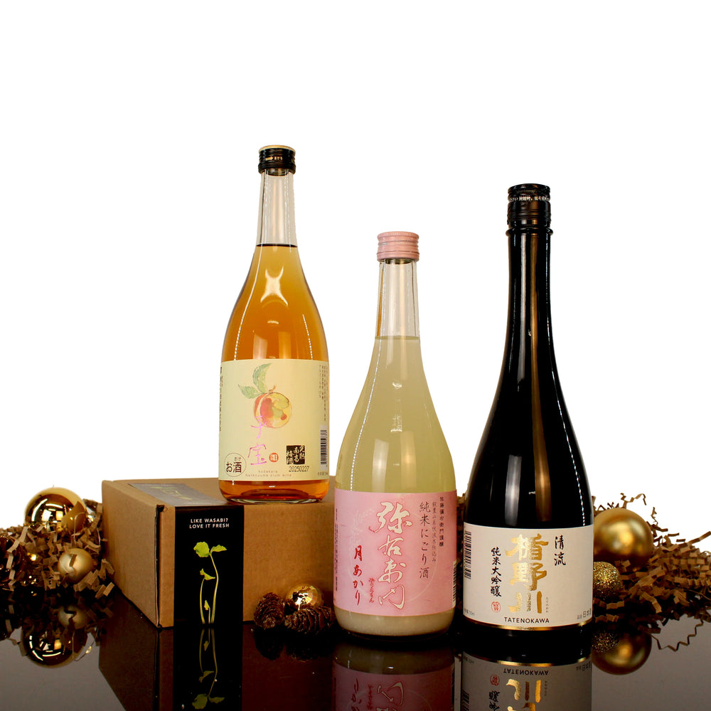 Three bottles from the Deluxe Sake Selection, each with decorative labels, are displayed before a gift box and gold accents—a perfect premium sake set for special occasions.